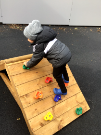 Child climbing small wooden climbing wall.