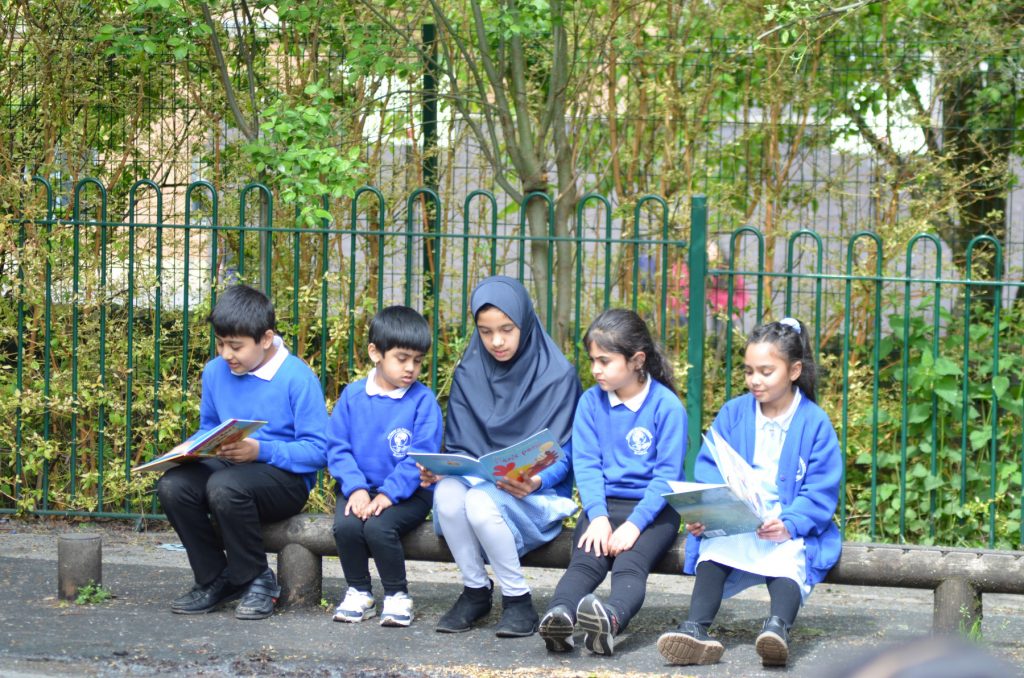 A group sitting on a outdoor balance beam reading picture  books.