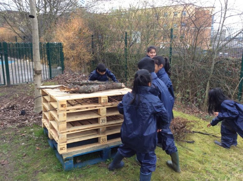 Children in overalls gathering sticks on to a pile of wooden pallets.