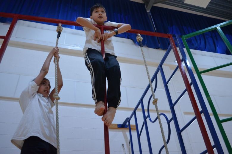 Two children at the top of gym ropes on colourful metal frames.