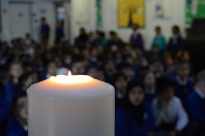 A lit candle in focus with assembly behind.