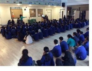 Children sitting in rows on the floor for collective worship.